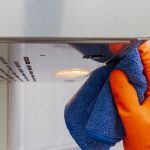 mana cu manusi de curatenie si laveta care curata o hota de grasime