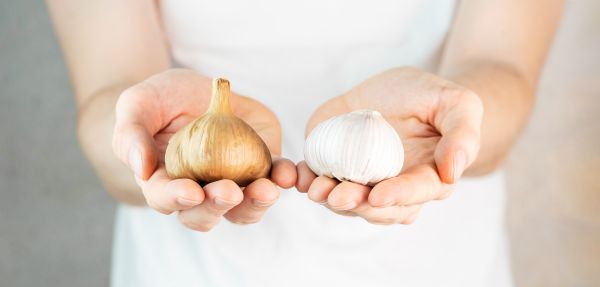 persoana care tine o capatana de usturoi intr-o mana, iar in cealalta mana o ceapa