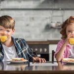 a little boy and a little girl having breakfast at the table, enjoying a glass of orange juice