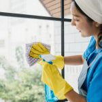 Femeie care curata geamurile cu o laveta si pulverizator cu solutie de curatat geamuri