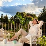 femeie relaxata pe un scaun pe balcon sub lumina soarelui de dimineata