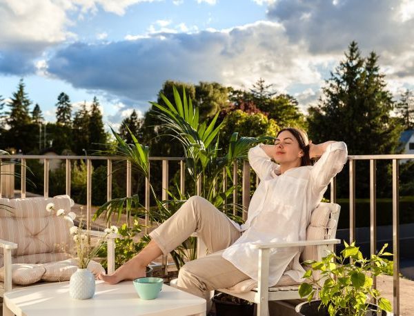 femeie relaxata pe un scaun pe balcon sub lumina soarelui de dimineata