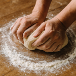 Hands kneading dough on a wooden board sprinkled with flour – symbol of basic doughs for bread, pies and pizza
